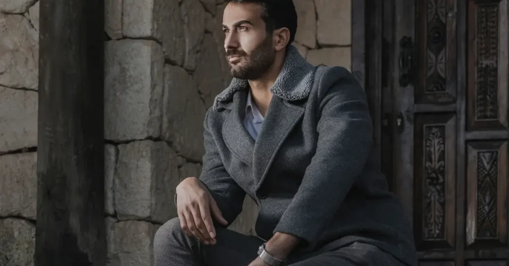 Man in gray winter coat contemplating in an old-world setting, showcasing winter fashion for men.
