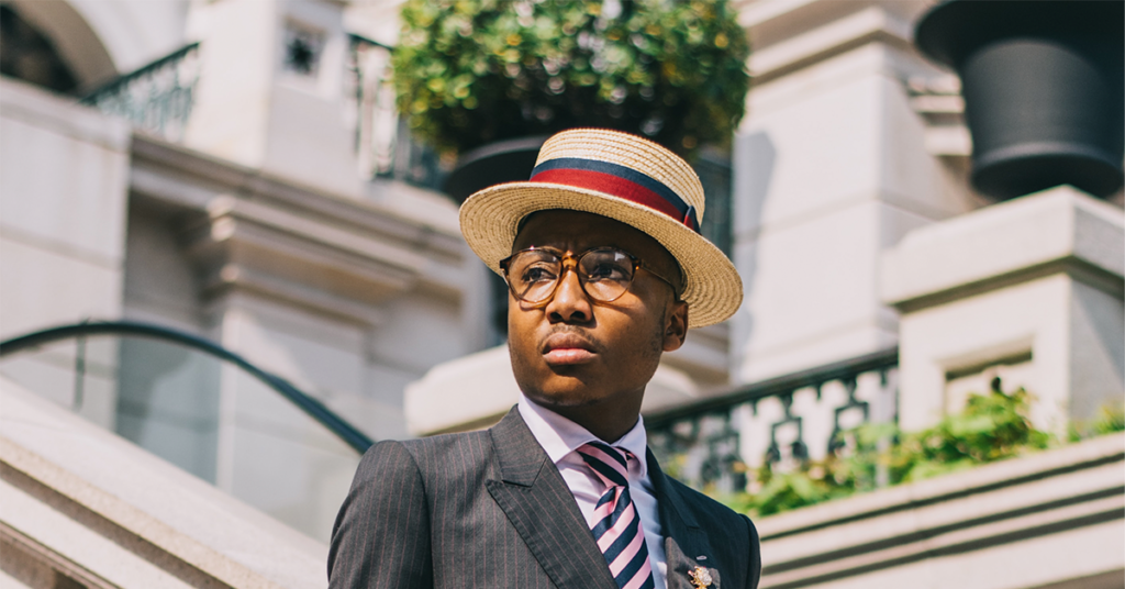 Elegant man in a pinstripe suit and striped hat, epitome of old money men's fashion.